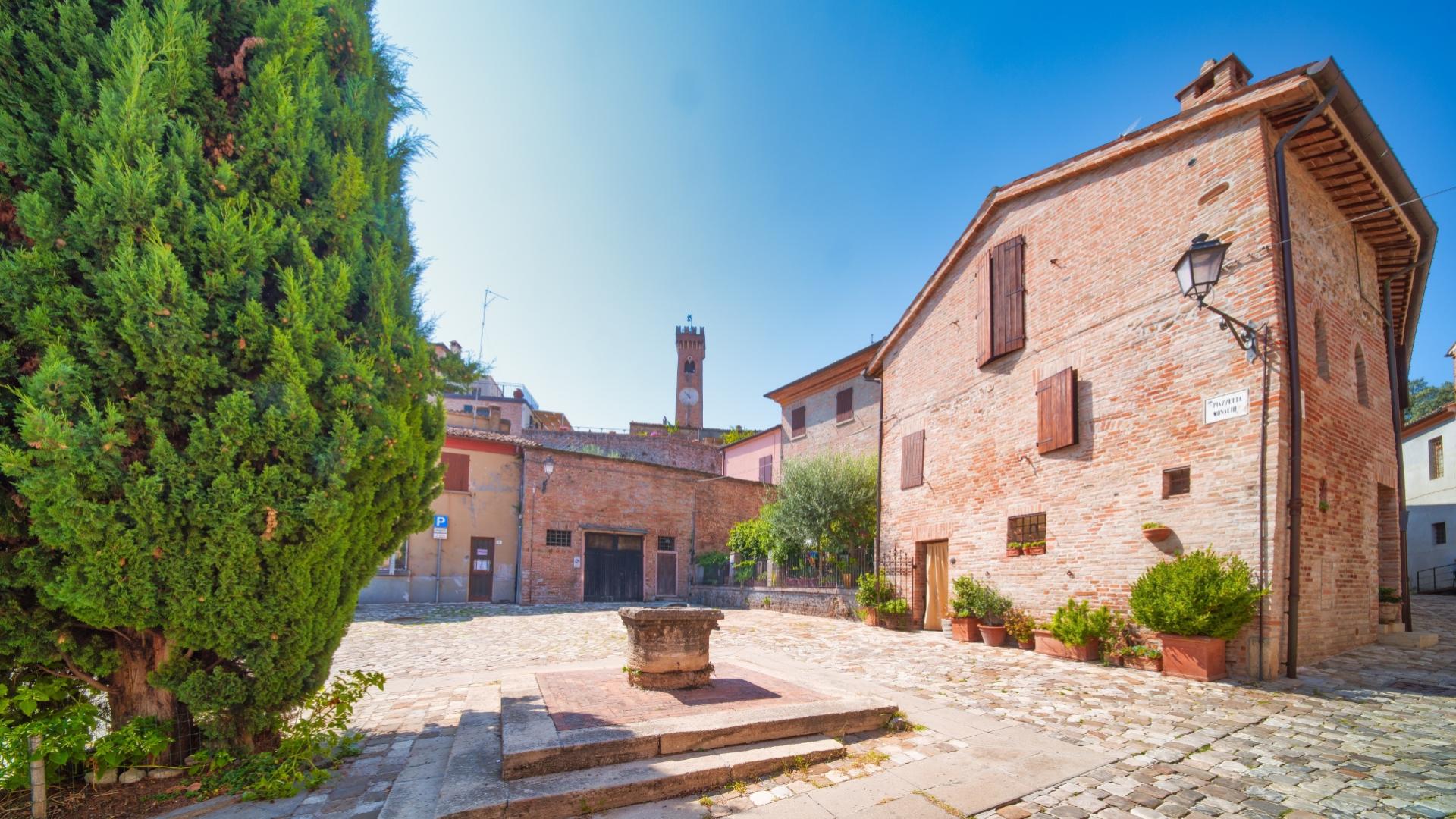 Piazza tranquilla con pozzo, edifici in mattoni e torre con orologio.