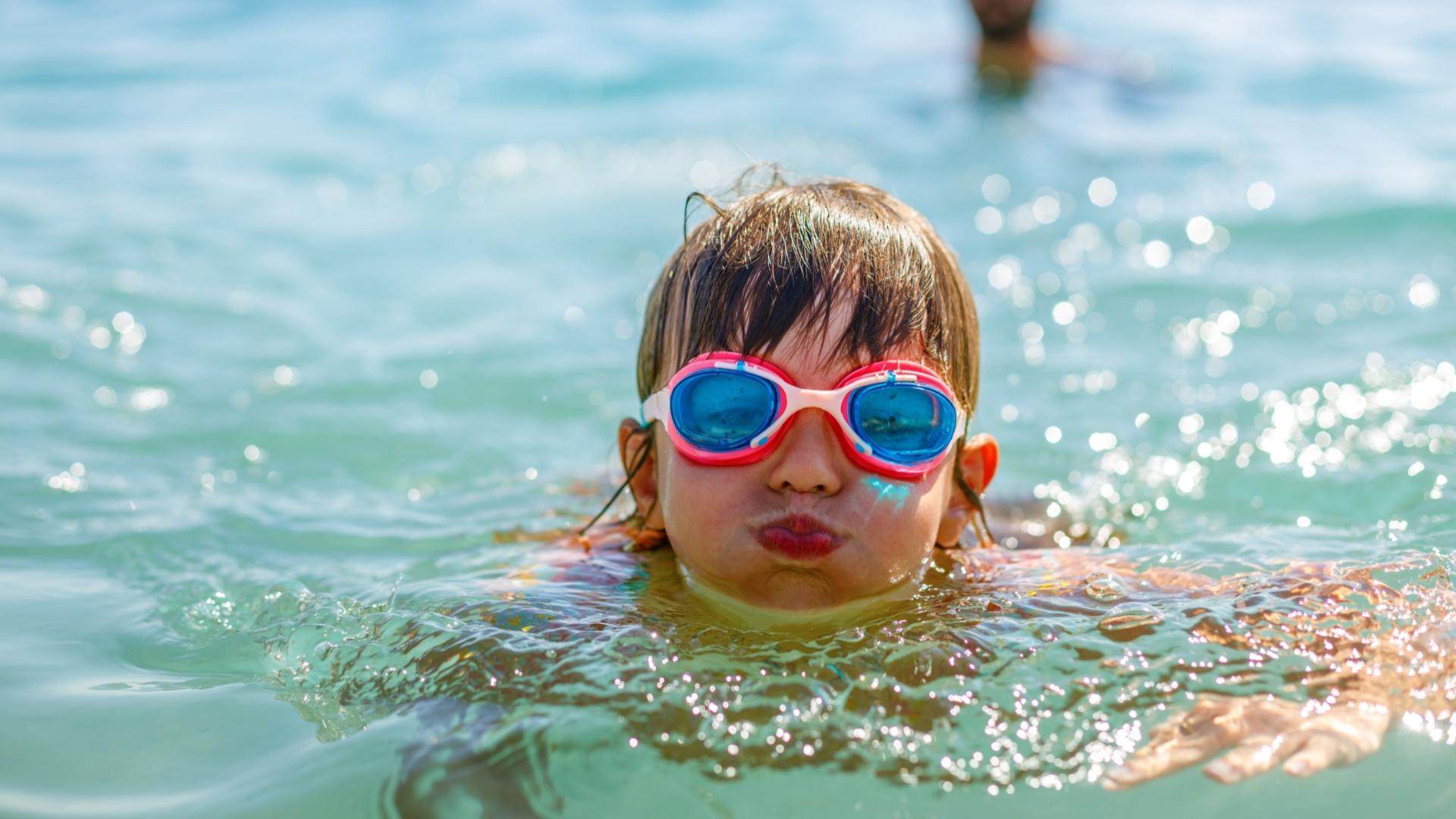 Bambino nuota con occhialini colorati in acqua limpida e soleggiata.