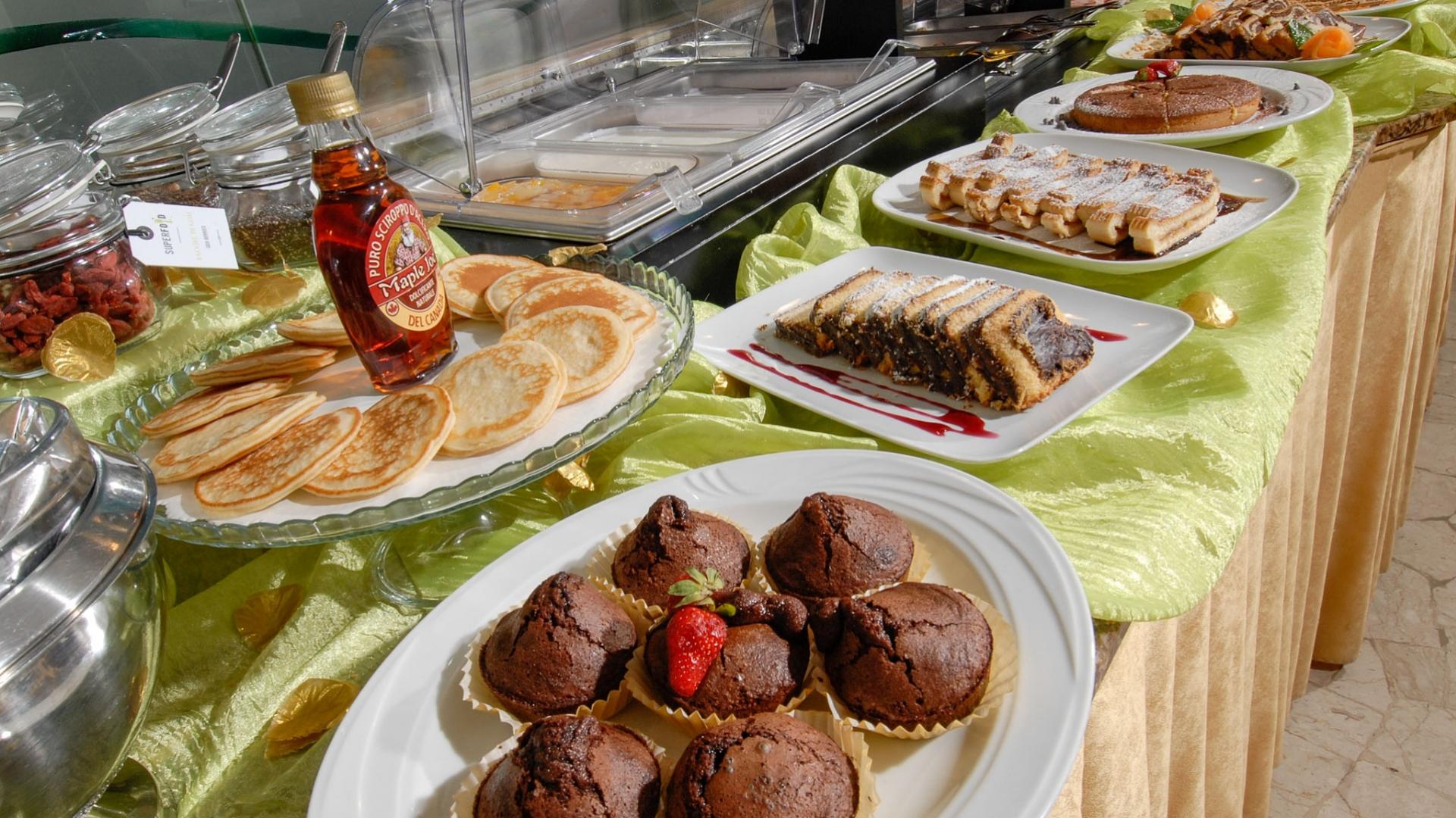 Buffet dolci con pancake, sciroppo d'acero, muffin al cioccolato e dolci assortiti.