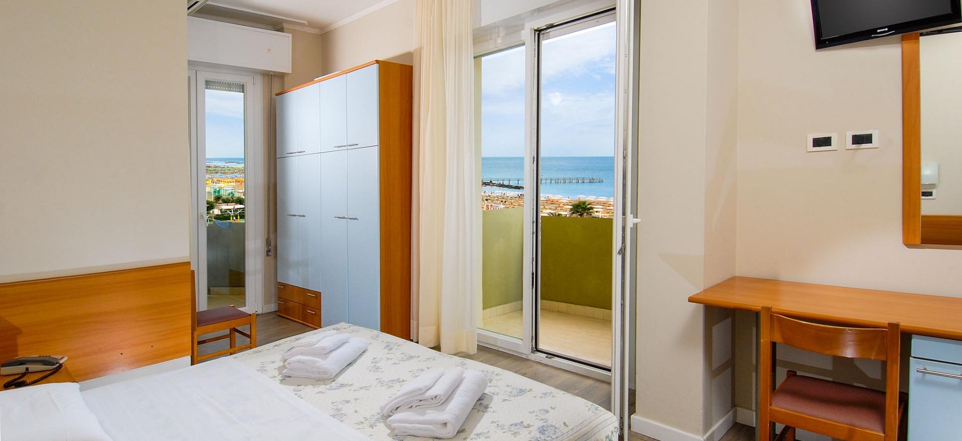 Camera d'hotel con vista mare, balcone, letto matrimoniale e arredamento semplice.