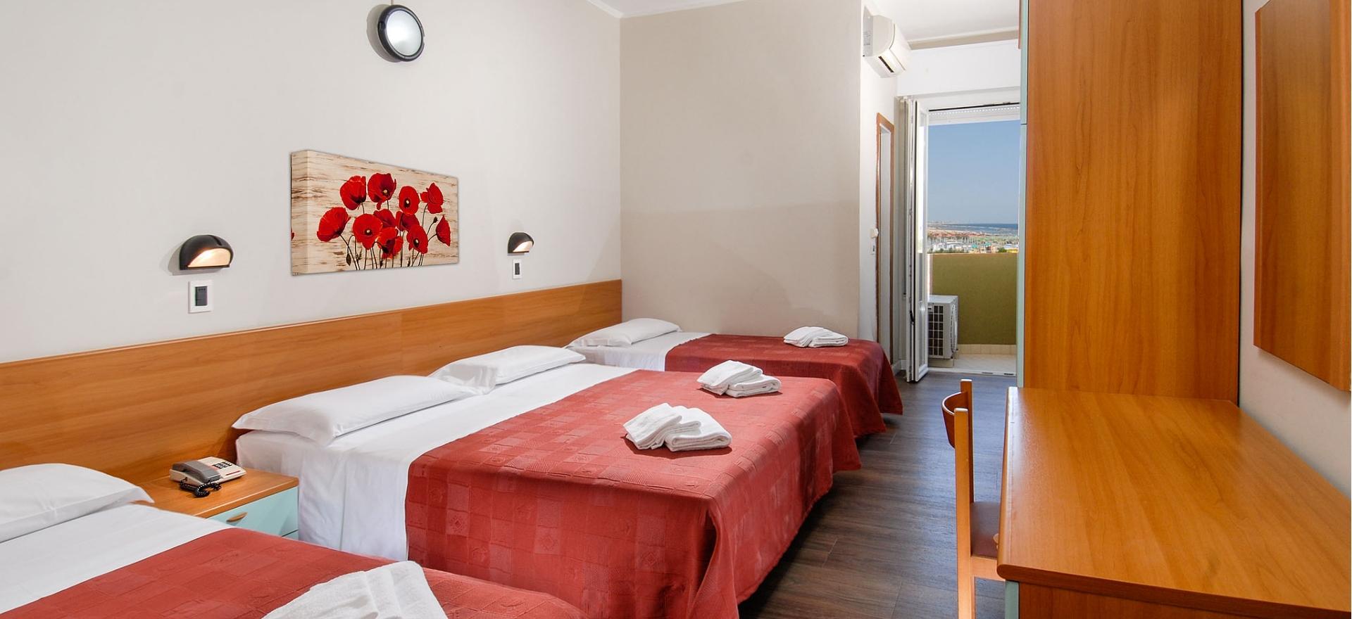 Camera d'albergo con tre letti singoli e vista sul mare.