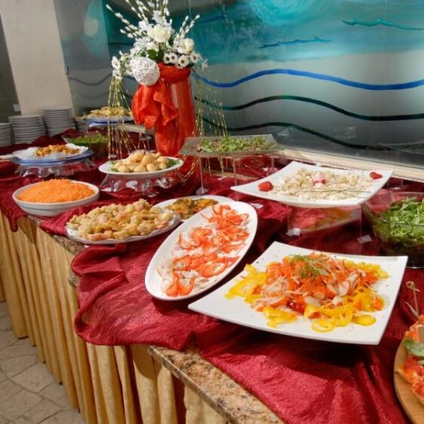 Buffet con piatti di pesce, insalate e pizza, decorato con fiori.