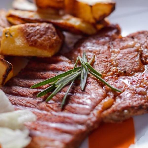Bistecca alla griglia con patate arrosto e rametto di rosmarino.
