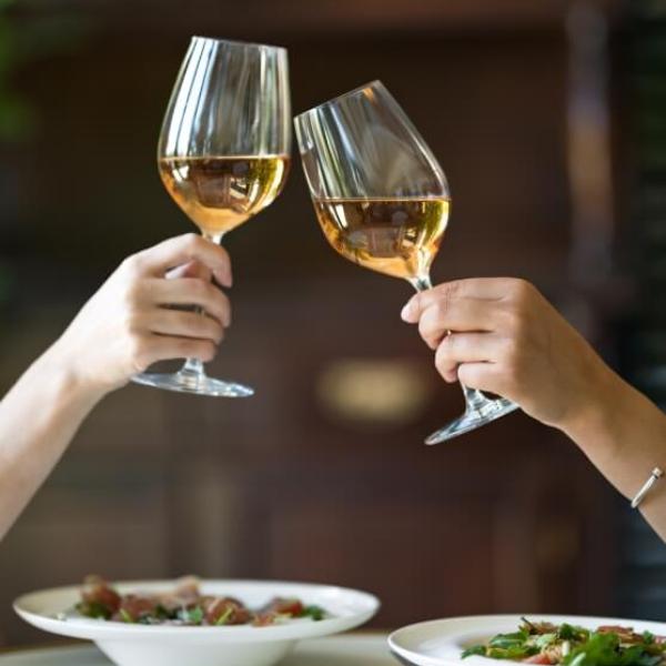 Due persone brindano con calici di vino bianco sopra un tavolo apparecchiato.