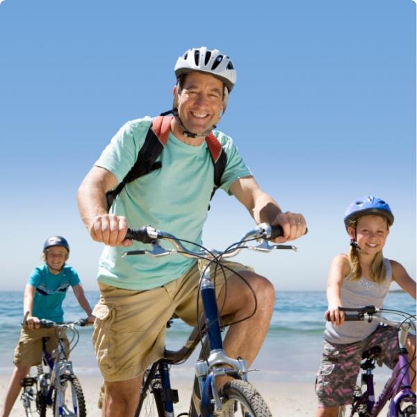 Famiglia in bicicletta sulla spiaggia, sorridente, con caschi e zaini.