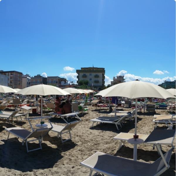 Spiaggia affollata con ombrelloni e sdraio sotto un cielo sereno e soleggiato.