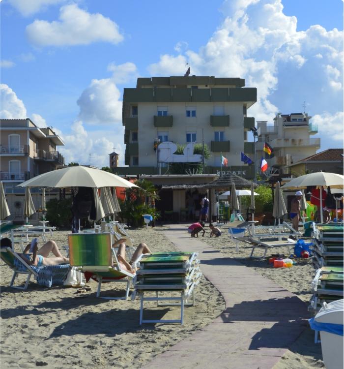 Spiaggia con lettini, ombrelloni e un edificio sullo sfondo, giornata soleggiata.